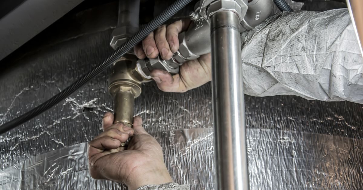 A plumber's hands installing and tightening pipe fittings with a spanner during a repair