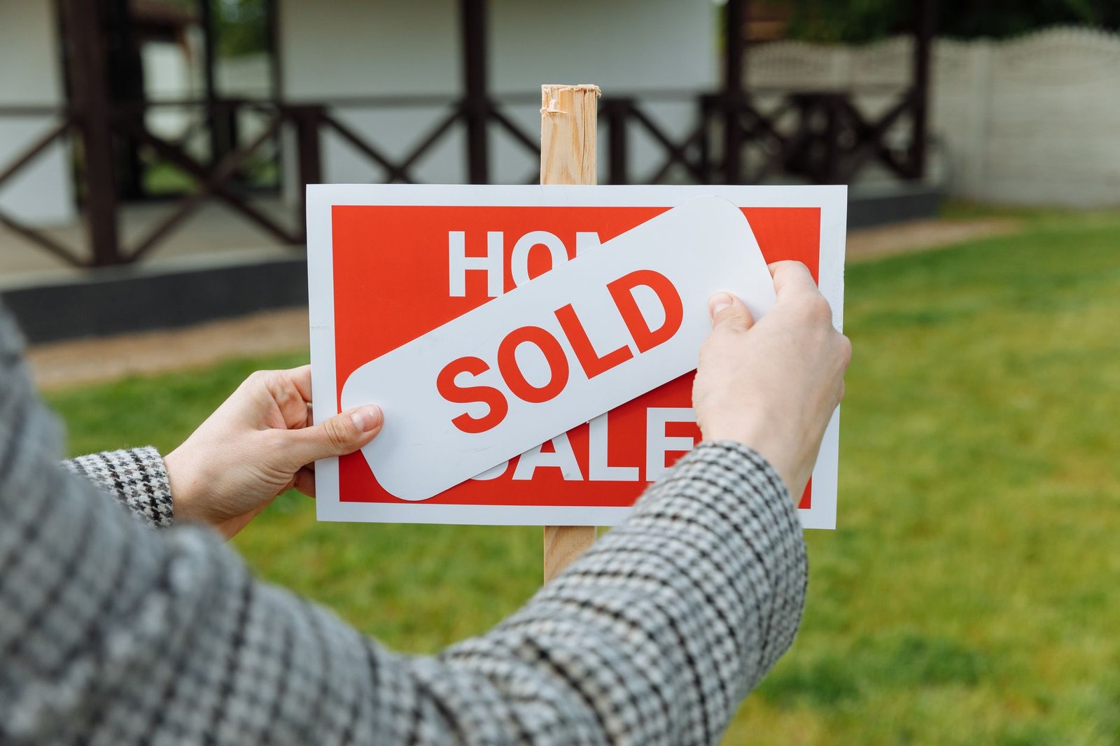 Hands placing a sold sticker onto a real estate sign outside a house