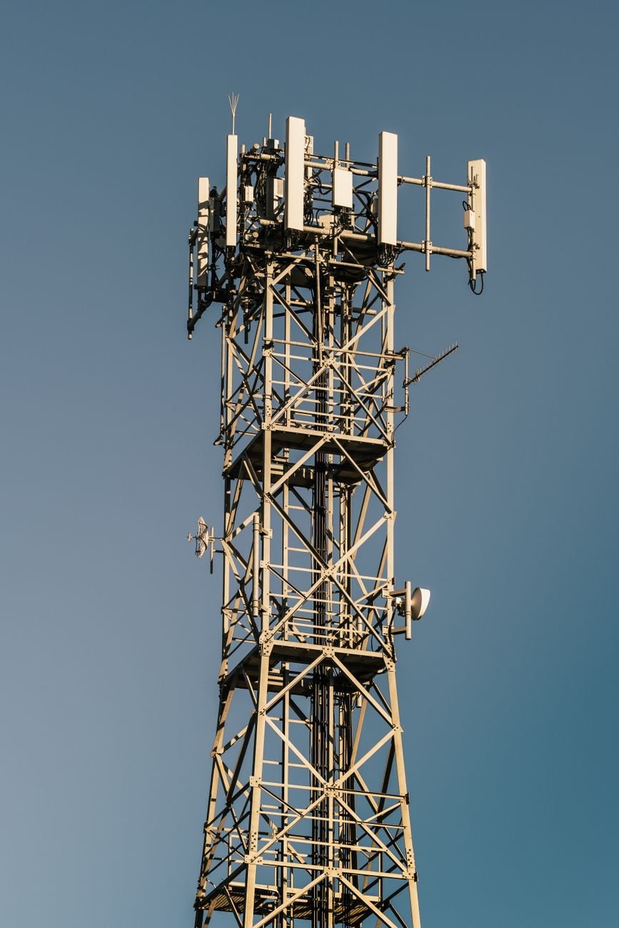 A 5G telecommunications tower fitted with panel antennas against a clear blue sky